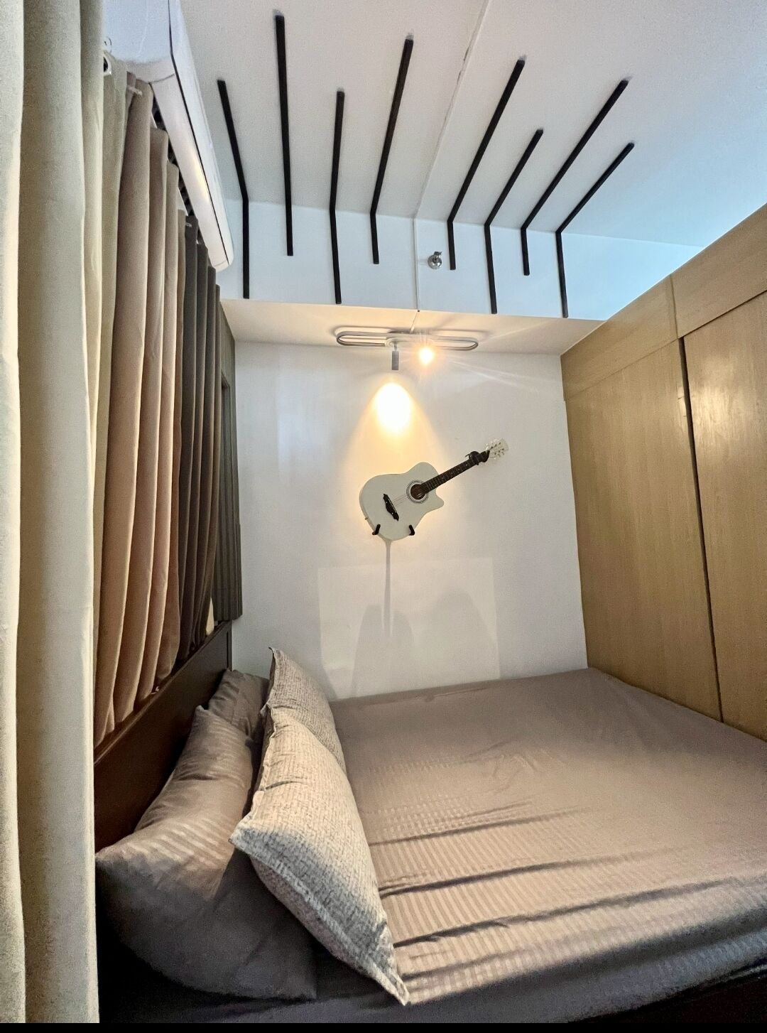A compact bedroom with a bed, pillows, a guitar, and a ceiling light fixture.