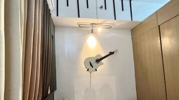 A compact bedroom with a bed, pillows, a guitar, and a ceiling light fixture.