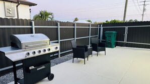 Une terrasse extérieure équipée d’un barbecue, de chaises et d’une poubelle.