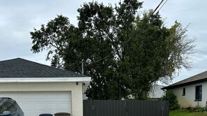 Une maison d’habitation avec un garage, un grand arbre et une clôture.