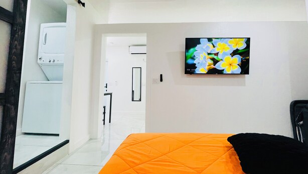 Une chambre à coucher avec un lit, un téléviseur fixé au mur et un lave-linge dans la pièce adjacente.