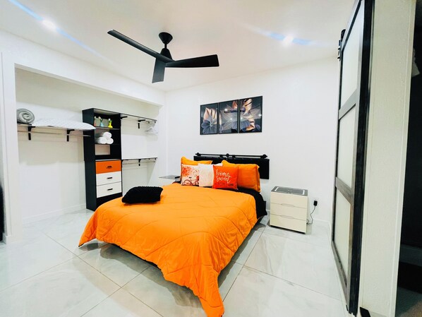 A bedroom with a bed, a ceiling fan, a wardrobe, a nightstand, and a wall-mounted artwork. - Magnolias Suite (Lehigh Acres)