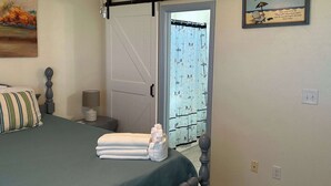 A bedroom with a bed, a nightstand, a lamp, a towel, a ceiling fan, and a beach-themed sign. - Villa Cape San Blas - Gulf View Townhome, Steps from the Beach & Local Dining (cape san blaste)