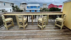 A wooden deck with four chairs and a table, overlooking a row of colorful houses. - Villa Cape San Blas - Gulf View Townhome, Steps from the Beach & Local Dining (cape san blaste)