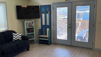 Een woonkamer met een zwarte bank, een televisie, een boekenkast en een deur die naar een balkon leidt.