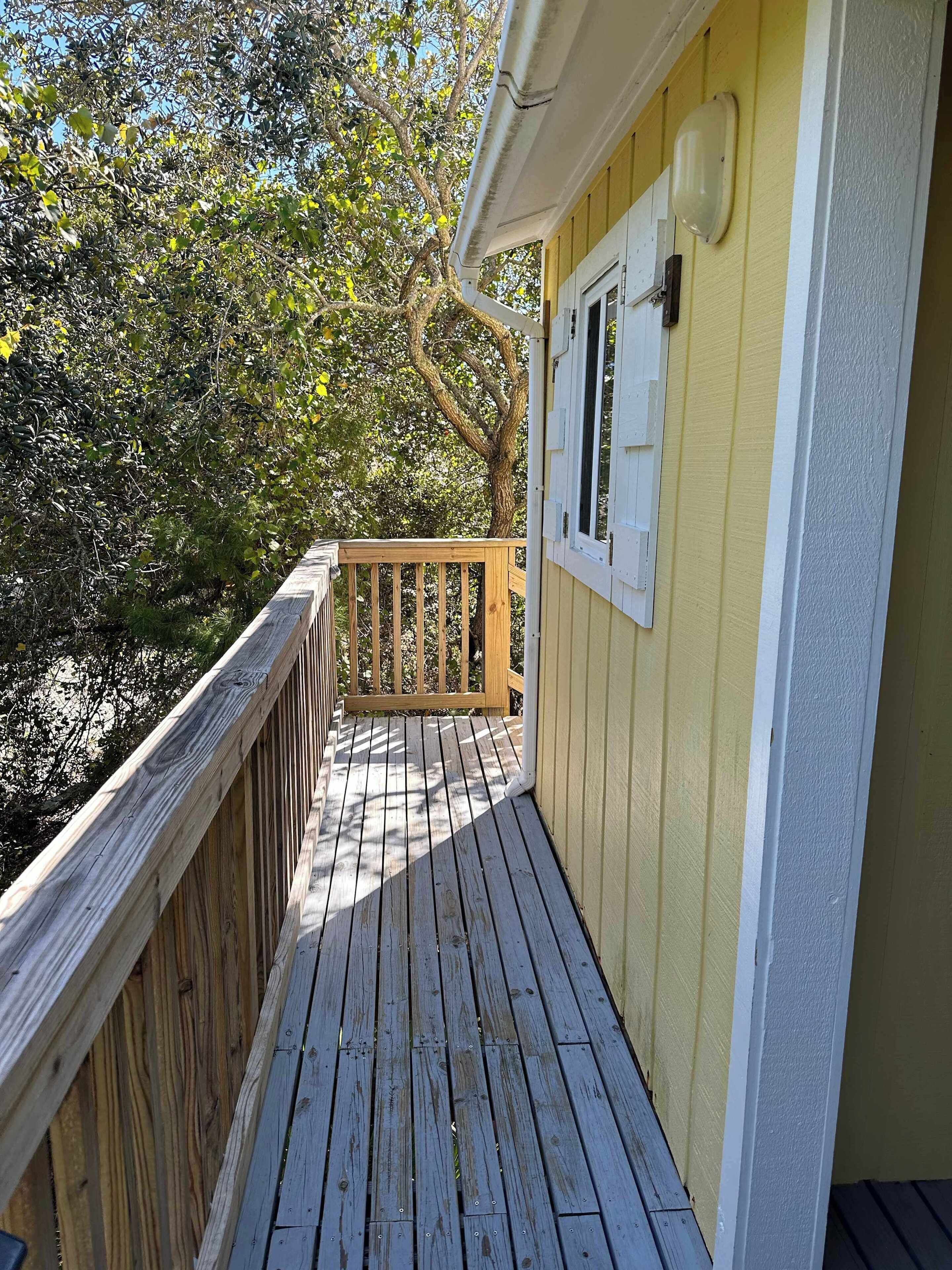 A wooden deck with a railing, a window, and a wall painted yellow.