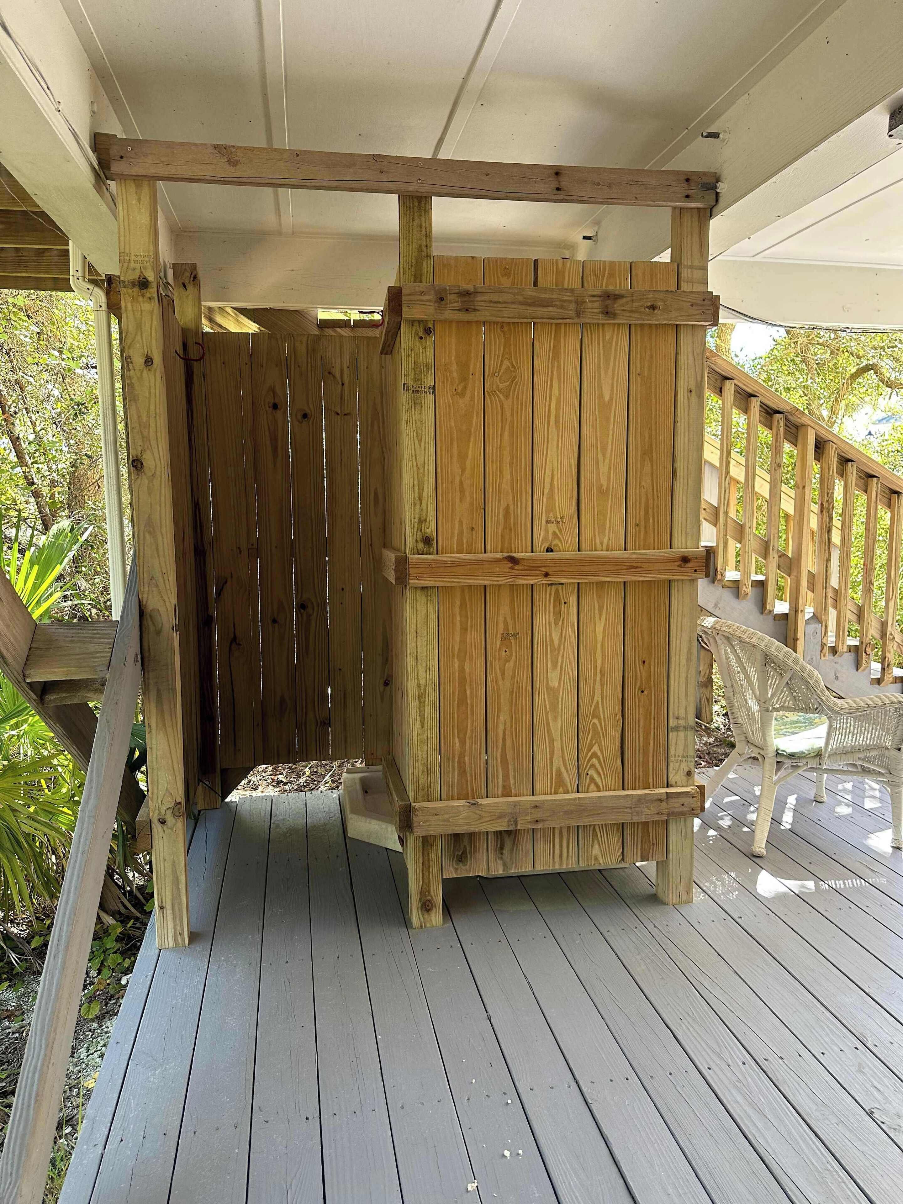 A wooden deck with a wooden gate, a wicker chair, and a white railing.