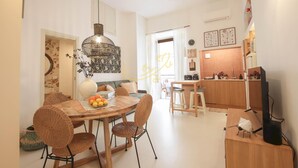 A modern dining area with a round wooden table, wicker chairs, and a hanging light fixture. - TD Casa Brunetti Heart of Historic Center (Monopoli)