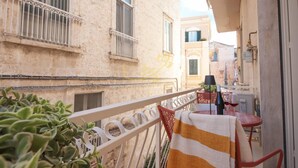 A narrow balcony with a striped towel, a small table with a bottle and glass, and a potted plant. - TD Casa Brunetti Heart of Historic Center (Monopoli)