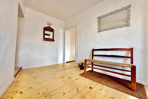 A hallway with wooden flooring, a bench, a mirror, and a door.