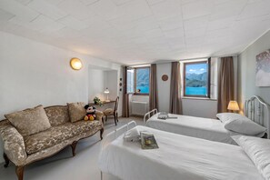 Ett hotellrum med en soffa, två sängar, ett fönster med utsikt över havet, en lampa och ett element.