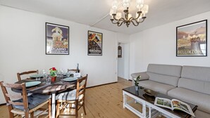 A dining area with a wooden table set for four, surrounded by chairs. A chandelier hangs from the ceiling, and there are posters on the walls. A sofa and a small table with a bowl and magazine are in the living area. - Casa Matilde 2 in Gerra Gambarogno, Gambarogno, Gerra, Switzerland (Gambarogno, Gerra)