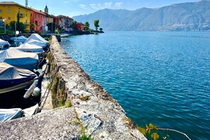 A waterfront with boats docked along a stone quay, buildings in the background, and mountains in the distance. - Casa Matilde 1 in Gerra Gambarogno, Gambarogno, Gerra, Switzerland (Gambarogno, Gerra)