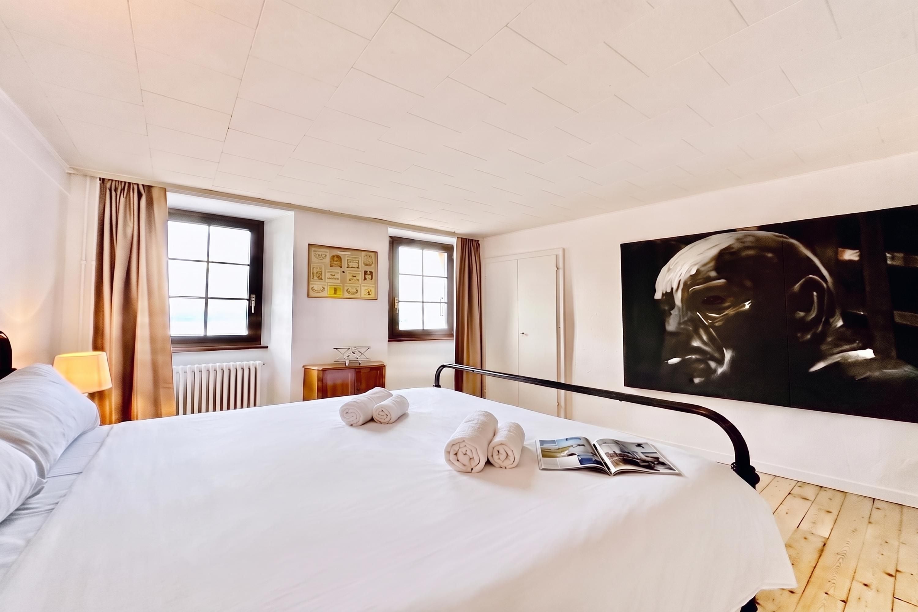 A hotel room with a bed, a large painting, and a window.