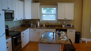 A kitchen with white cabinets, a granite countertop, a microwave, a stove, and a window with blinds.