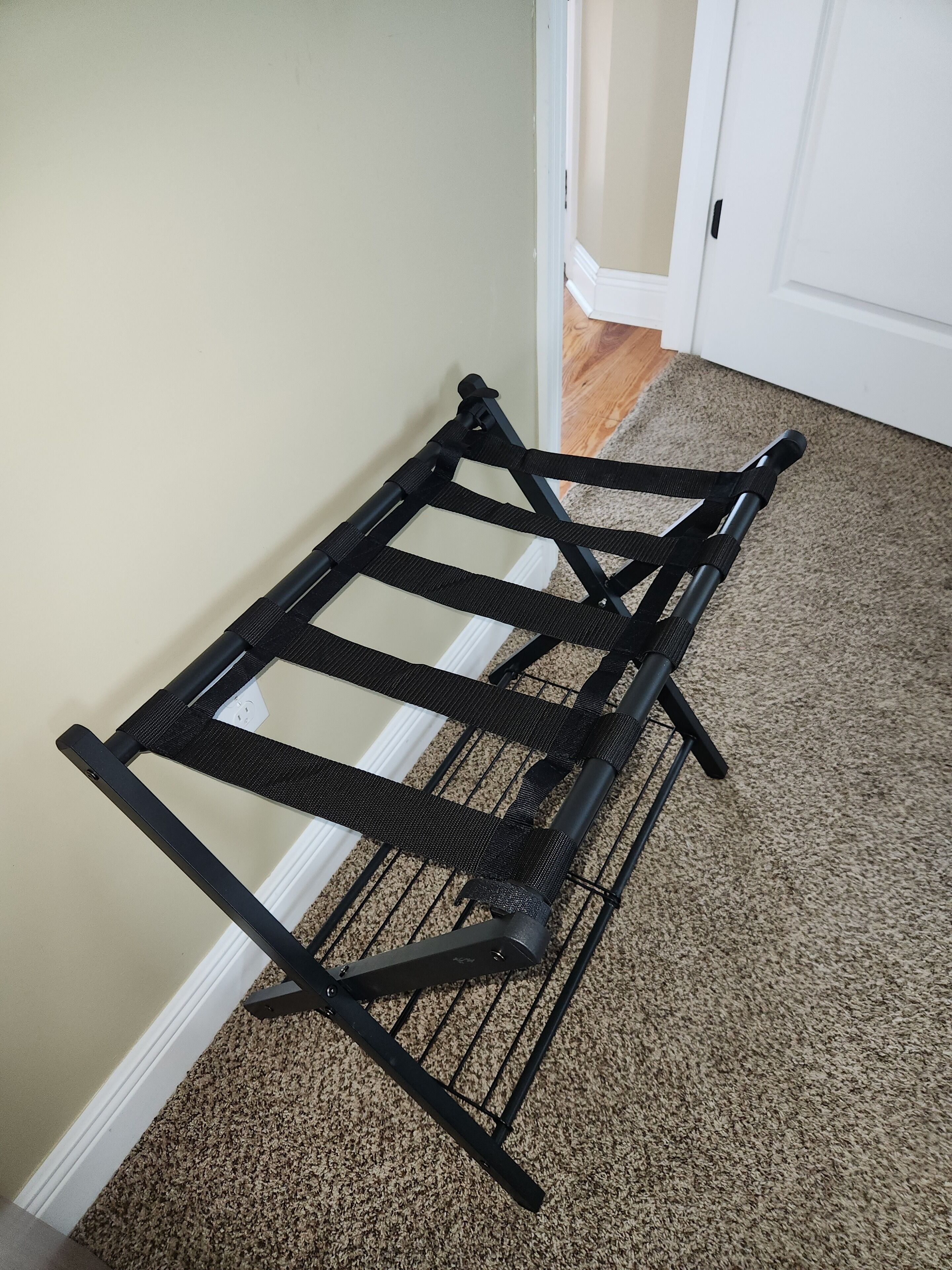 A black metal drying rack against a beige wall with a carpeted floor.