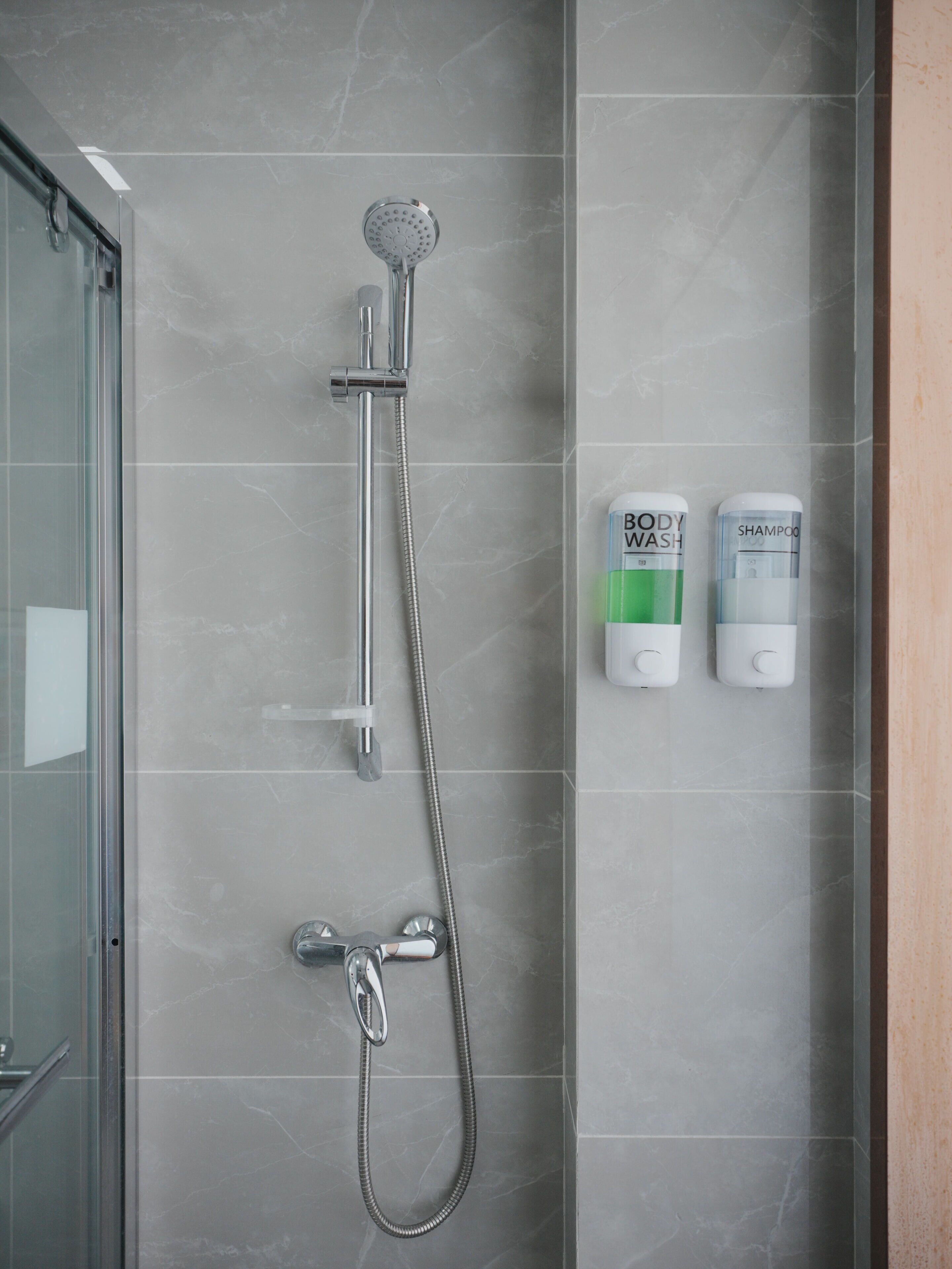 Ducha con cabezal de ducha de mano y grifo empotrado en la pared. Se observan dos botellas de jabón corporal y champú en la pared.