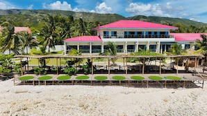 Un hotel con techo rojo, varios balcones y zona de estar exterior con cojines verdes.