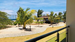 Un balcón con vista a una playa, palmeras y una estructura de techo de paja.