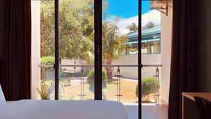 Habitación de hotel con una cama grande, un balcón que ofrece vistas a zonas verdes y un edificio, y un escritorio con una silla.