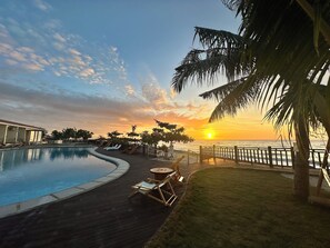A pool area with a view of the sunset over the ocean, surrounded by palm trees and lounge chairs. - W Golf Resort (Oslob)