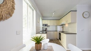 Una cucina moderna con mobili bianchi, un forno a microonde e un fornello. C'è un tavolo da pranzo con sedie e una pianta in vaso.