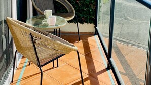 Un balcone con una parete verdeggiante, due sedie in vimini, un tavolino in vetro e vista su un edificio con un cartello 'NO PARKING'.