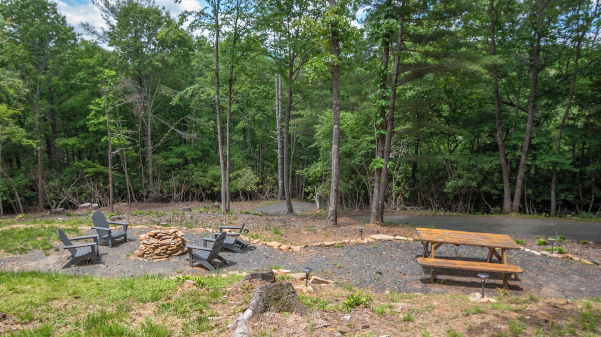A campsite with picnic tables, a fire pit, and a paved path.