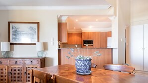 A dining area with a wooden table, chairs, a vase with flowers, and a kitchen in the background. - Breakers 1/10- Stone Real Estate Yamba (Yamba)