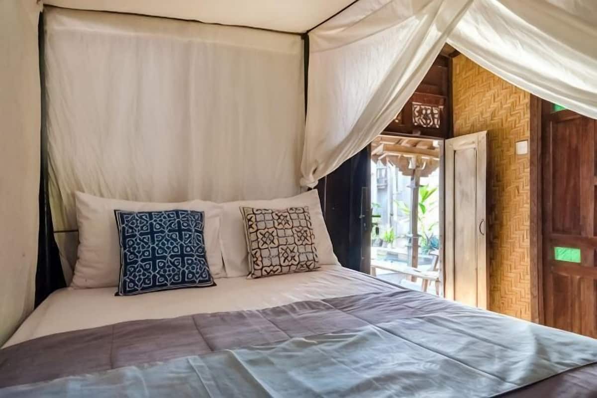 A bed with a canopy, patterned pillows, and a view of a wooden door and outdoor area.