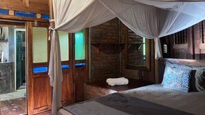 Una habitación con una cama, un armario de madera, una mesita y una ventana que da a un muro de ladrillo.