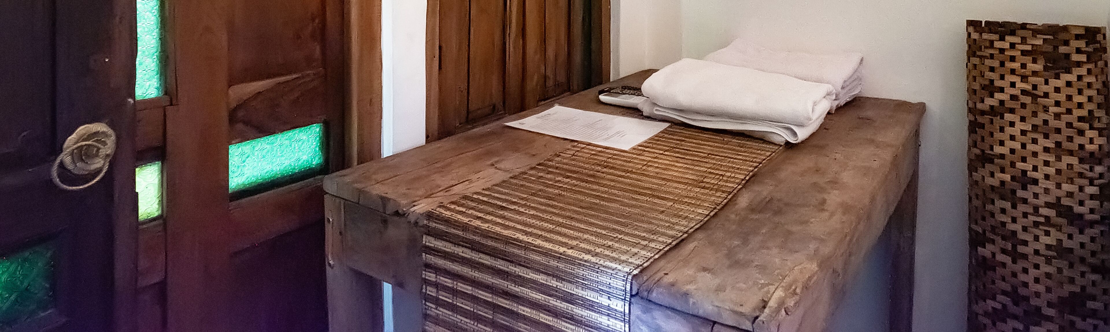 A wooden massage table with a folded towel and a piece of paper, possibly a receipt, on top.