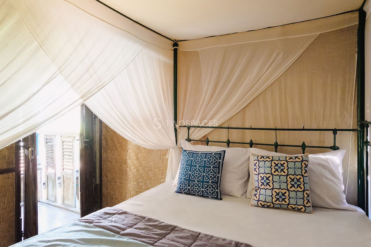 A bed with a canopy, two patterned pillows, and a view of a wooden door and wall.