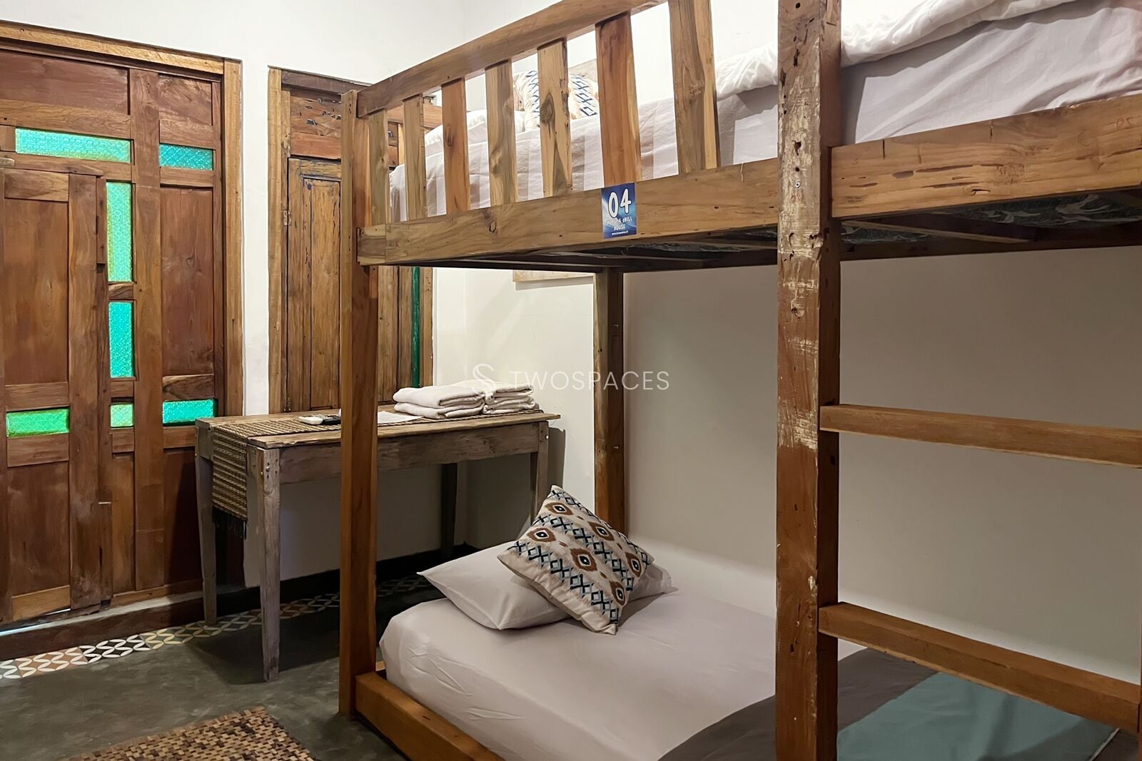 Een slaapkamer met een stapelbed, een houten bureau en een kussen met dessin.