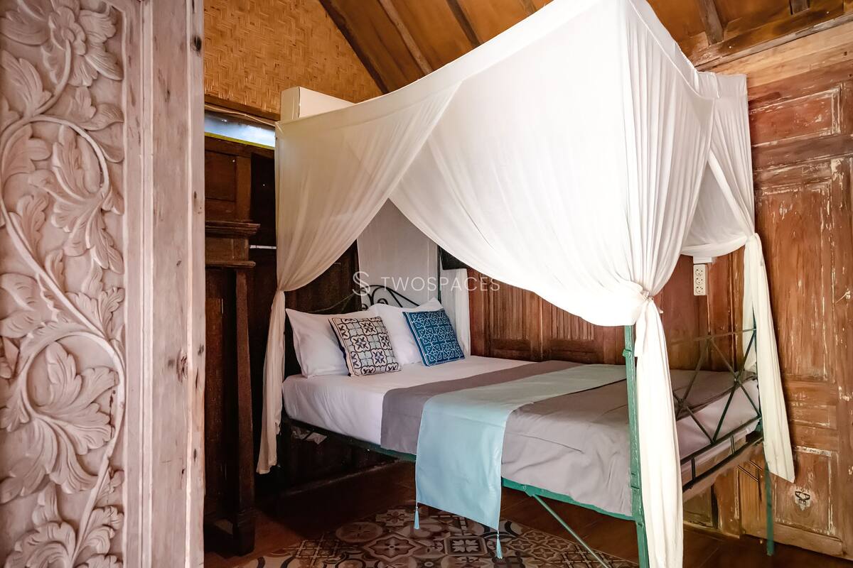 A wooden room with a bed under a white canopy, a patterned wall, and a small window.
