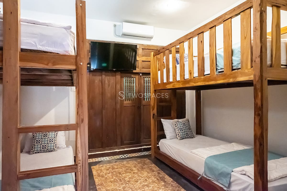 A bunk bed room with a television above the lower bunk, wooden walls, and a patterned rug.
