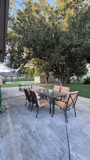 Patio esterno con tavolo e sedie, circondato da un albero e un recinto.