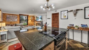 A modern kitchen with a central island, a dining area with a sofa, and a living room with a TV. - Stylish 2BR Walk to Ski Slopes (Park City)