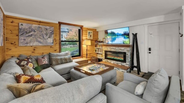 A modern living room with a fireplace, a large TV, and a cozy seating area. - Stylish 2BR Walk to Ski Slopes (Park City)