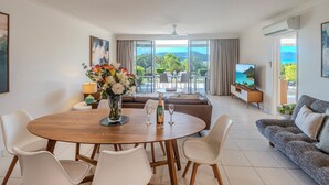 A modern living room with a round wooden table, white chairs, a sofa, and a TV. - Lagoon 004 by HamoRent on Hamilton Island (Hamilton Island)