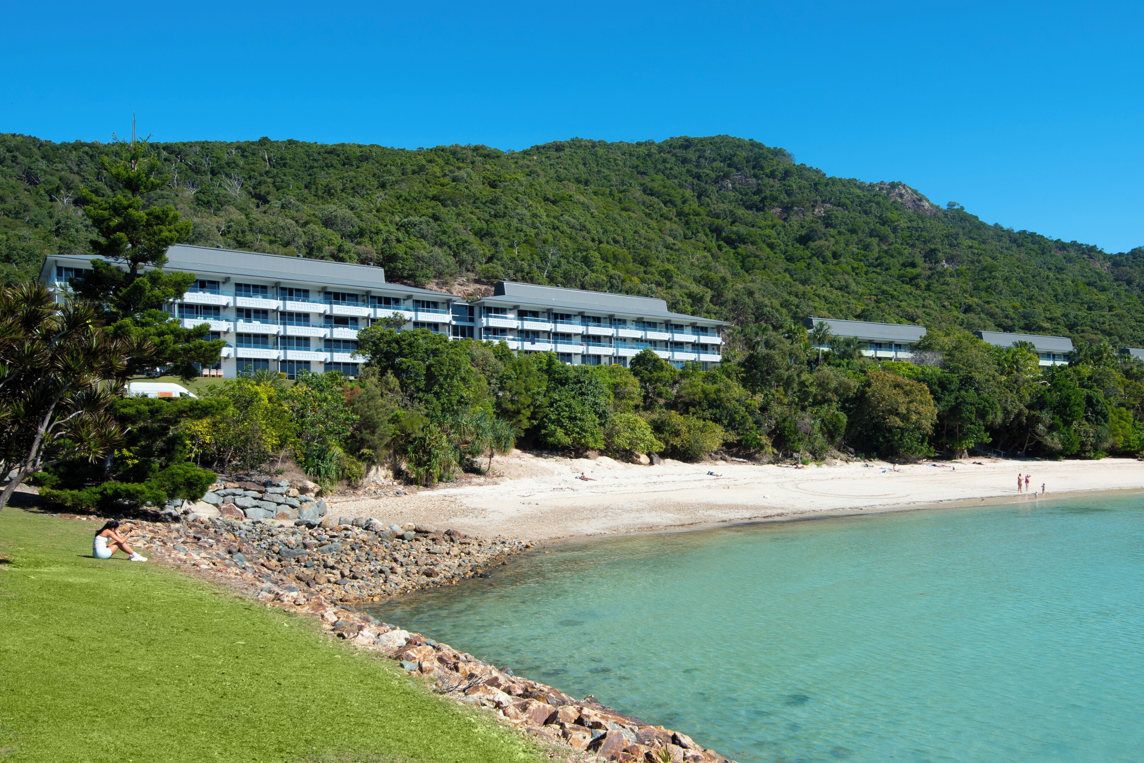 Un hotel frente a la playa con varias construcciones, una playa de arena y un mar azul cristalino.
