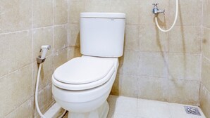 A small, white toilet with a bidet attachment in a tiled bathroom. - OYO Life 90388 De'leota (Semarang)