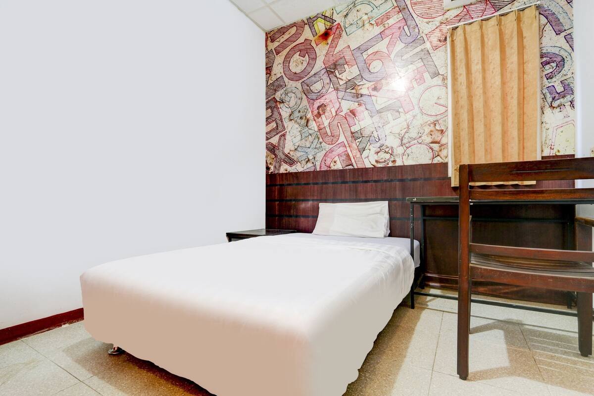 A hotel room with a bed, a wooden chair, and a wall with a patterned design.