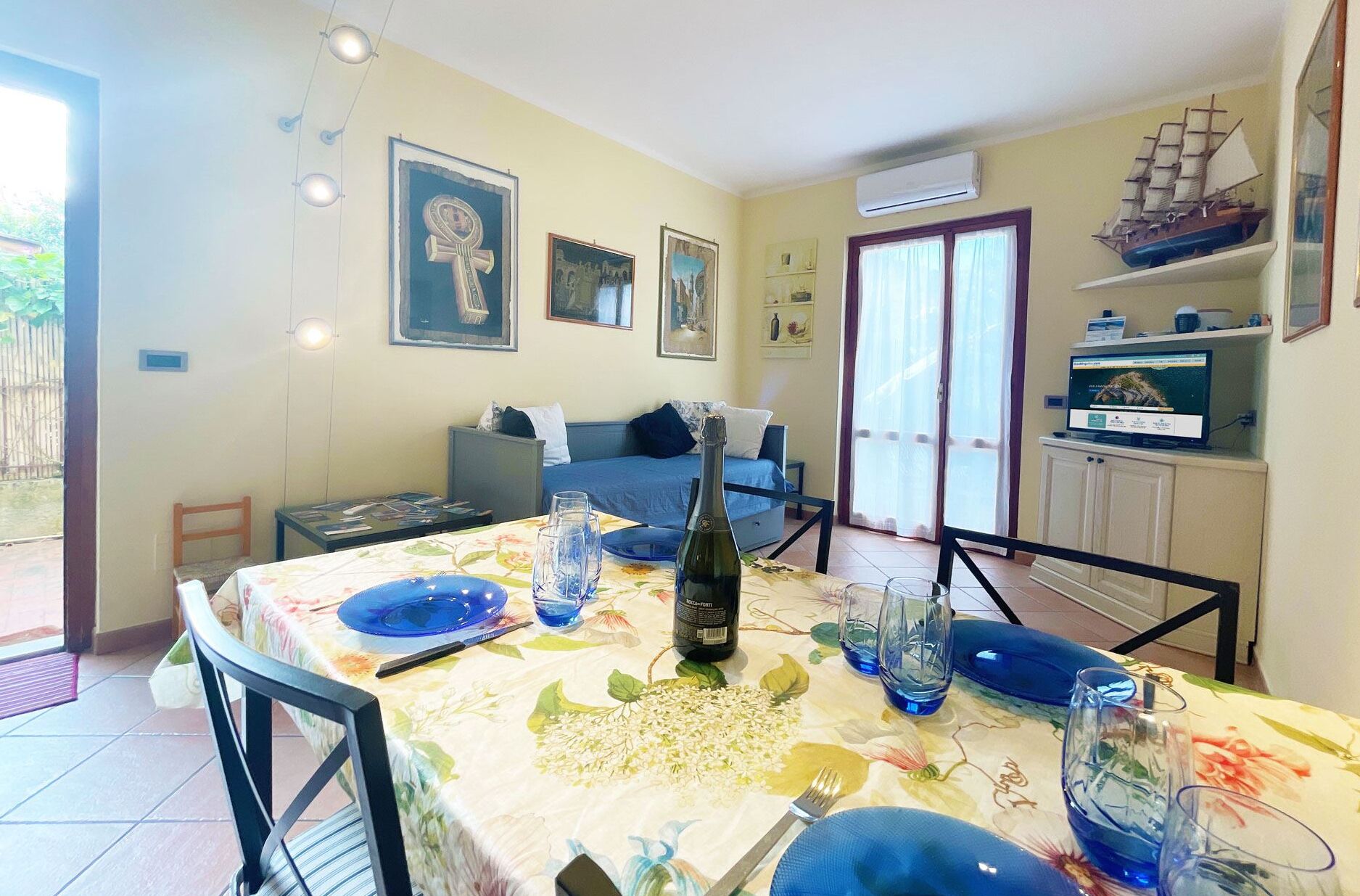A dining area with a table set for two, a bottle of wine, and a ship model on a shelf.