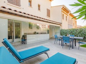 Un patio con sillones azules, una mesa de comedor con sillas y una cocina con paredes de vidrio.