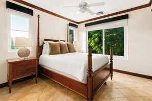 Une chambre à coucher avec un lit à baldaquin, une table de chevet, une lampe et une vue sur la verdure par la fenêtre.