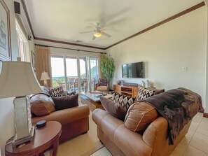 A living room with leather sofas, a TV, and a ceiling fan.