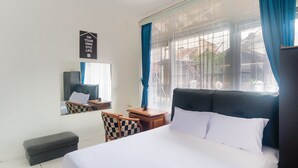 Una camera d'albergo con un letto, una sedia, un tavolino, uno specchio e una finestra con tende.