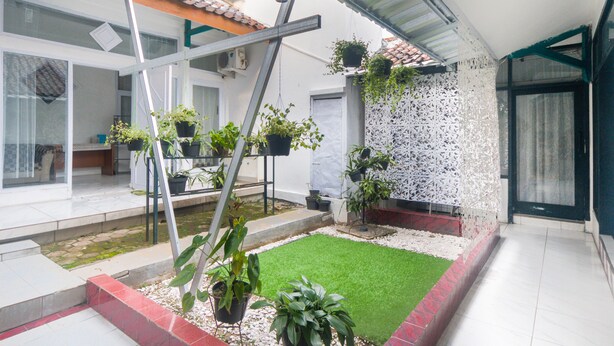 Un cortile con prato verde, piante in vaso, un muro decorativo bianco e una scala in metallo.