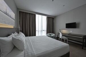 A hotel room with a bed, a desk, a chair, a TV, and a window with curtains.